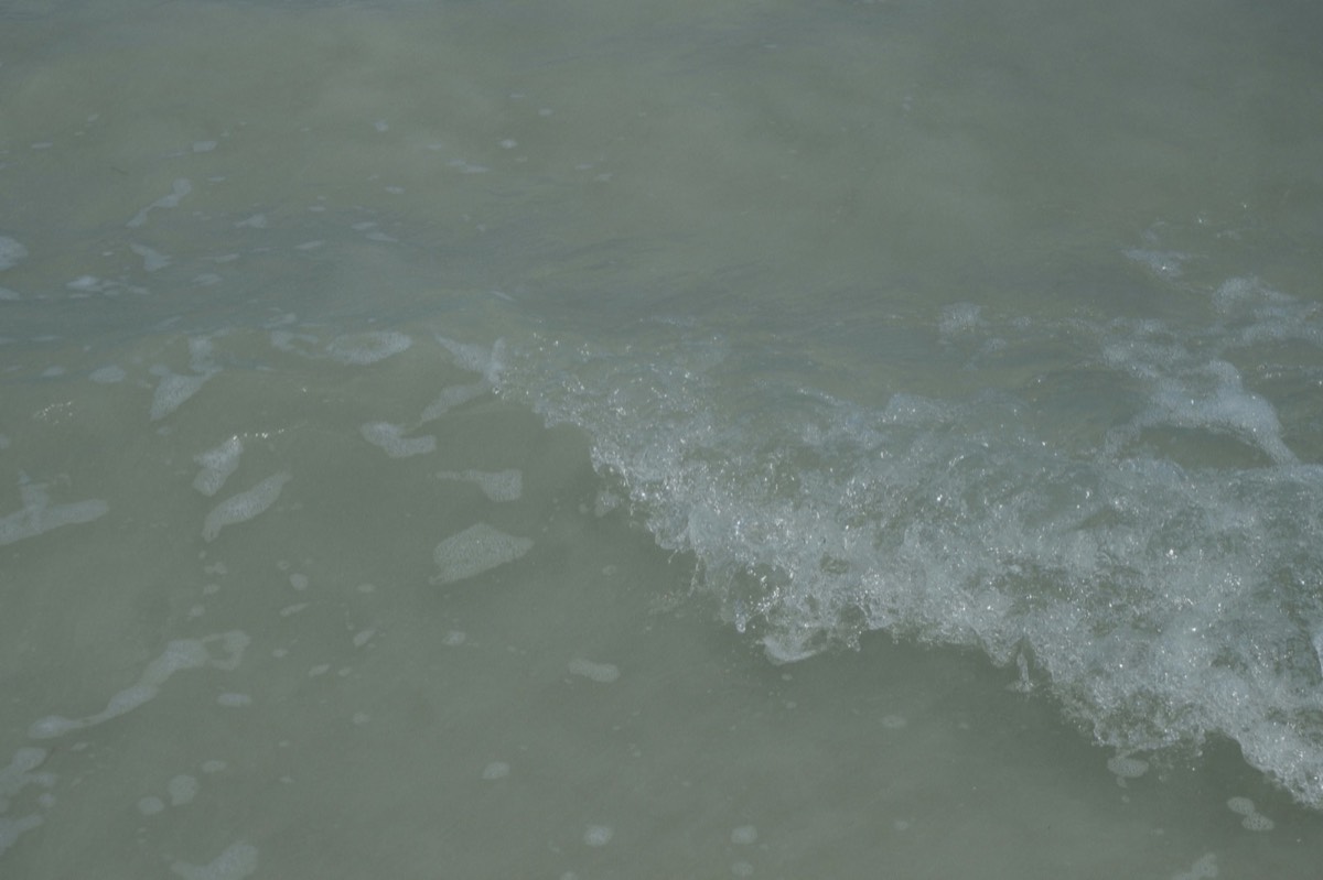 Uma onda suave a quebrar numa praia de areia tranquila com luz suave do dia: o treino vesical reformula a urgência como uma onda, não como uma falésia